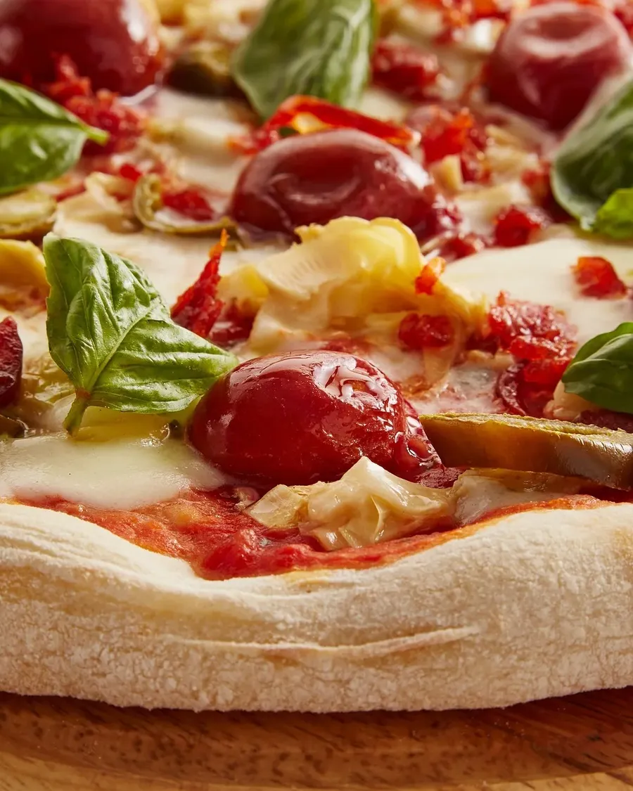 Pizza crust and toppings of basil, tomato and artichoke, close up